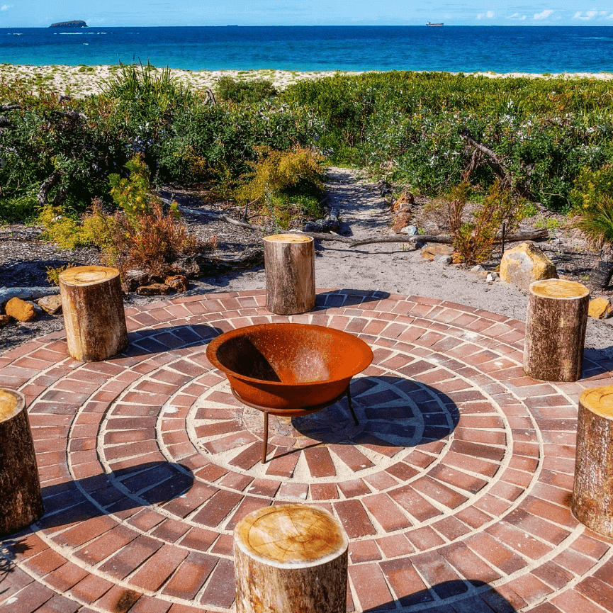 Fire pit with wooden tree stumps around it over looking the beach