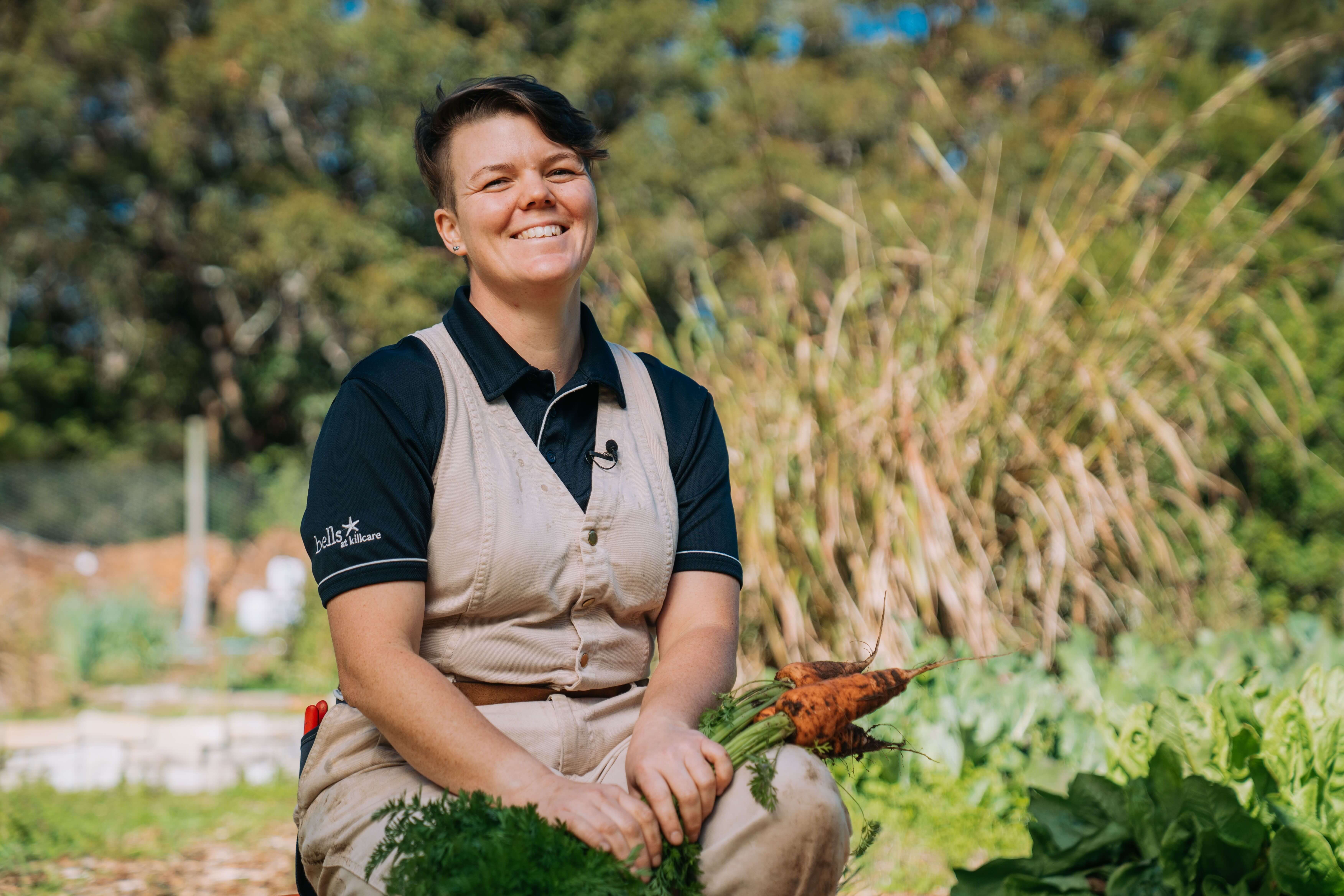 the head horticulturalist smiling in their onsite garden harvesting produce