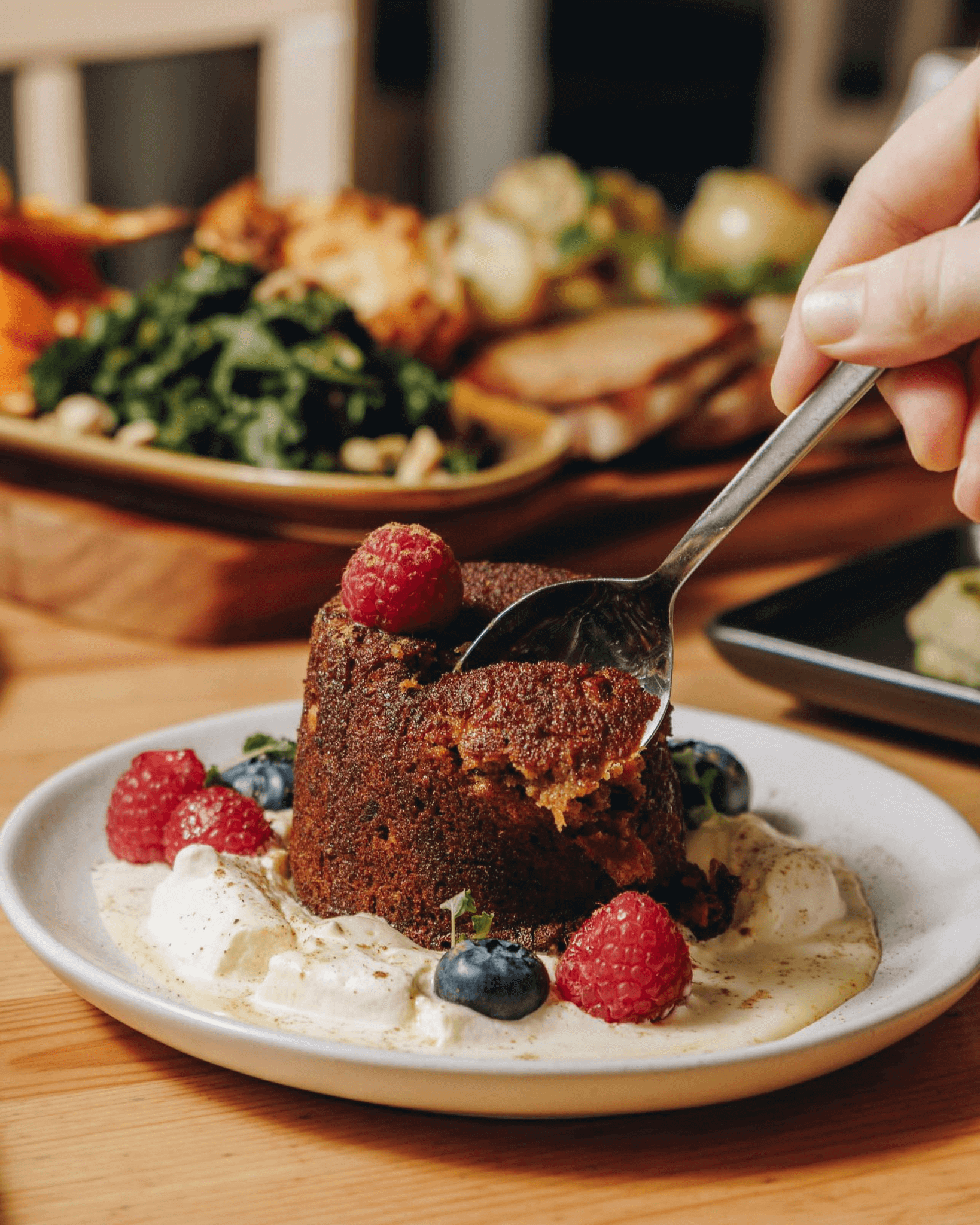 Person cutting into a christmas pudding with raspberries and blueberries and cream