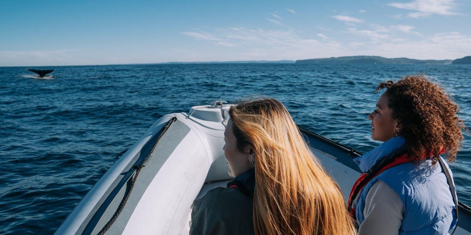 Two women in a boat watching a whale breach the water