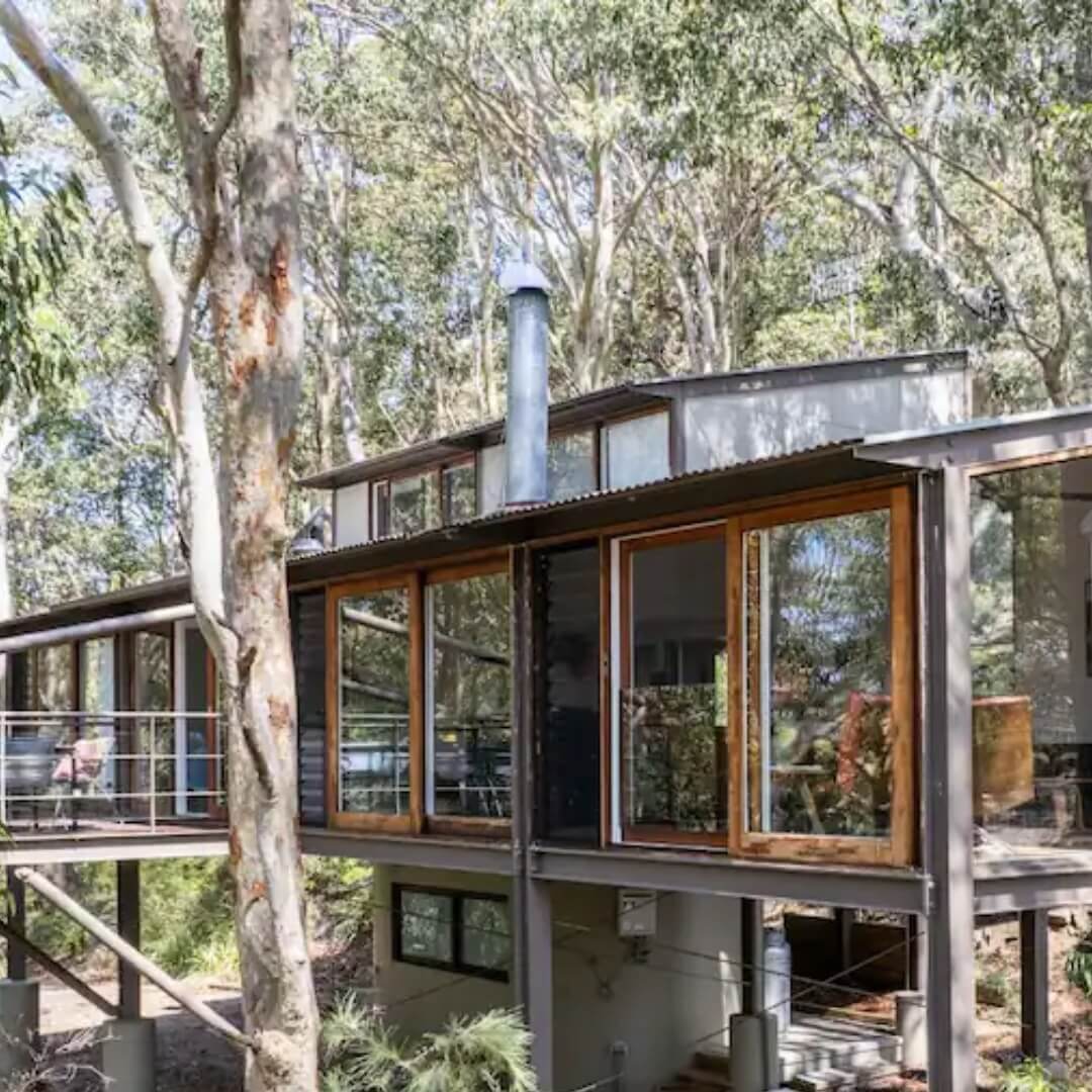 An industrial looking cabin sitting on stilts amongst the lush canopy of eucalyptus trees in Bouddi National Park.