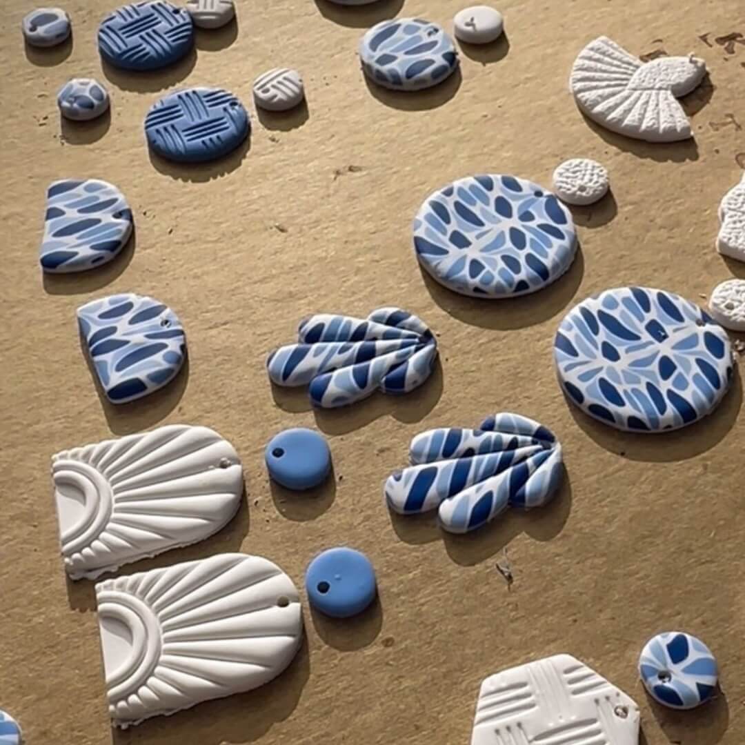 A collection of cut-out polymer clay earrings with varying cobalt blue and cream patterns and shapes.
