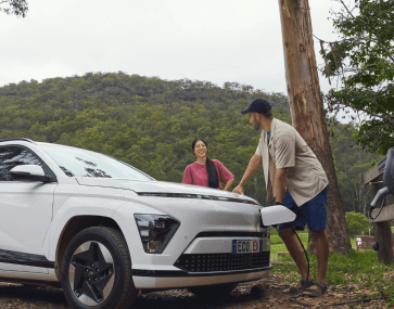 two people leaning on an ev charging car