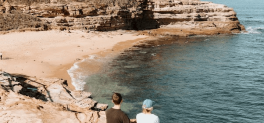 2 people sitting on rock overlooking coastline